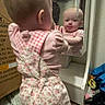 baby, mirror, reflection, clothing, pink, overalls, standing, tongue_out, carpet, box, room, furniture, child, curious, indoor, person, baby_girl, playful, face, expression