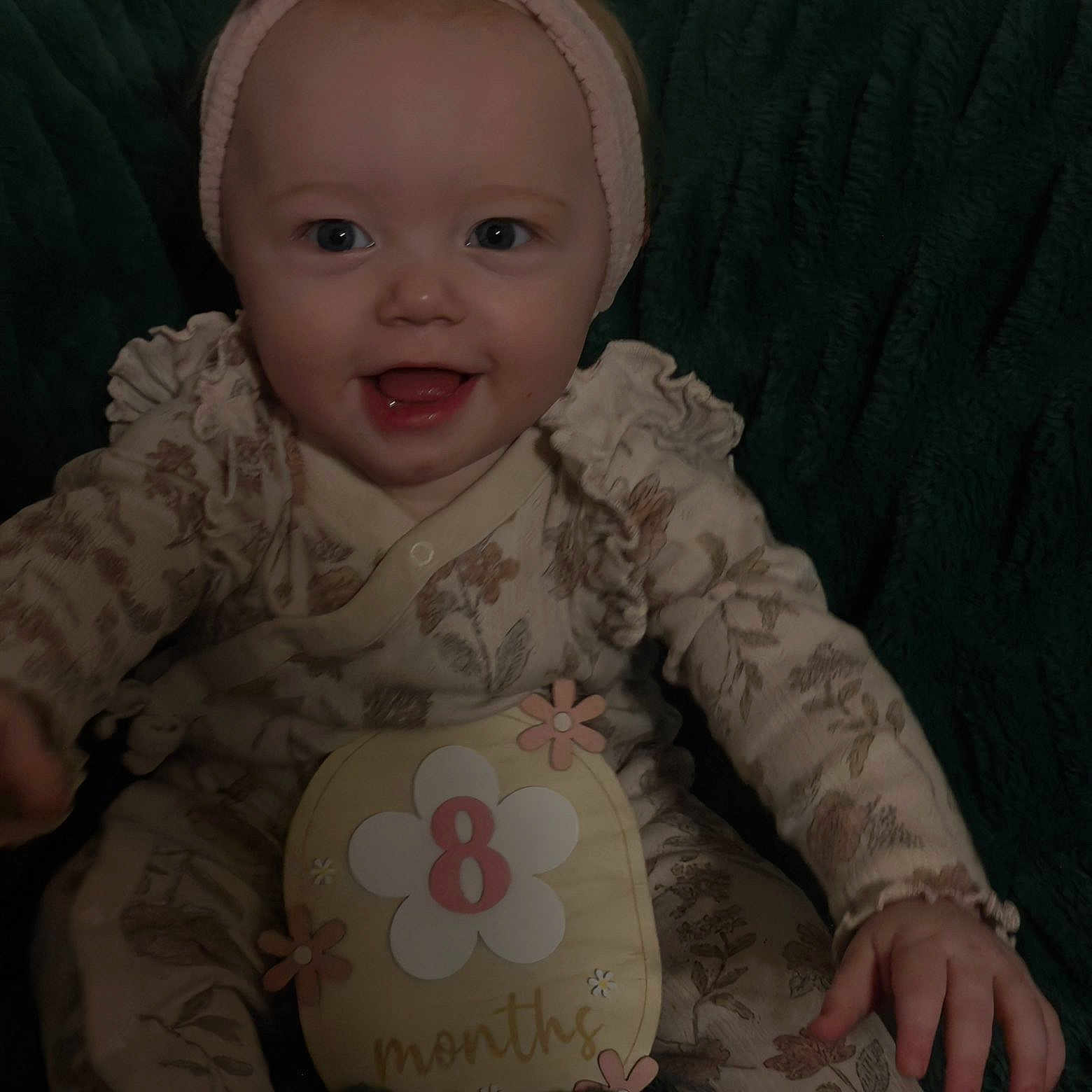 Lilly is registered to the contest to win money with this photo: baby, child, smiling, onesie, headband, infant, portrait, face, hand, flower, months, sitting, cute, happy, clothing, background, texture, young, person, indoor