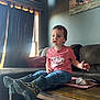 toddler, child, indoor, living_room, table, boots, rain_boots, pink_shirt, curtains, sofa, carpet, wooden_floor, window, natural_light, portrait, expression, decor, photograph, toy, rock