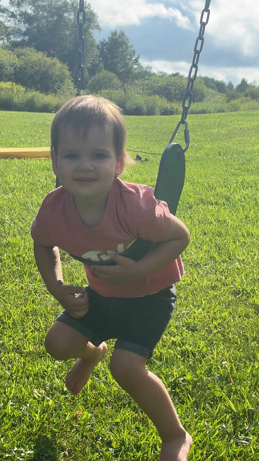 Lanie is registered to the contest to win money with this photo: child, toddler, swing, playground, grass, outdoor, summer, sunlight, greenery, smile, barefoot, shorts, tshirt, happy, nature, sky, clouds, play, fun, daytime