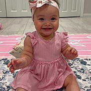 Eliana is registered to the contest to win money with this photo: baby, child, girl, smiling, pink_dress, headband, bow, sitting, floor, quilt, floral_pattern, indoors, happy, cute, toes, arms, face, eyes, hair, mouth
