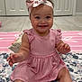 baby, child, girl, smiling, pink_dress, headband, bow, sitting, floor, quilt, floral_pattern, indoors, happy, cute, toes, arms, face, eyes, hair, mouth