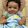 baby, smiling, curly_hair, blanket, blue_blanket, baby_seat, infant, cute, child, portrait, happy, face, hands, cozy, toddler, indoor, soft_texture, patterned_blanket, closeup, playful