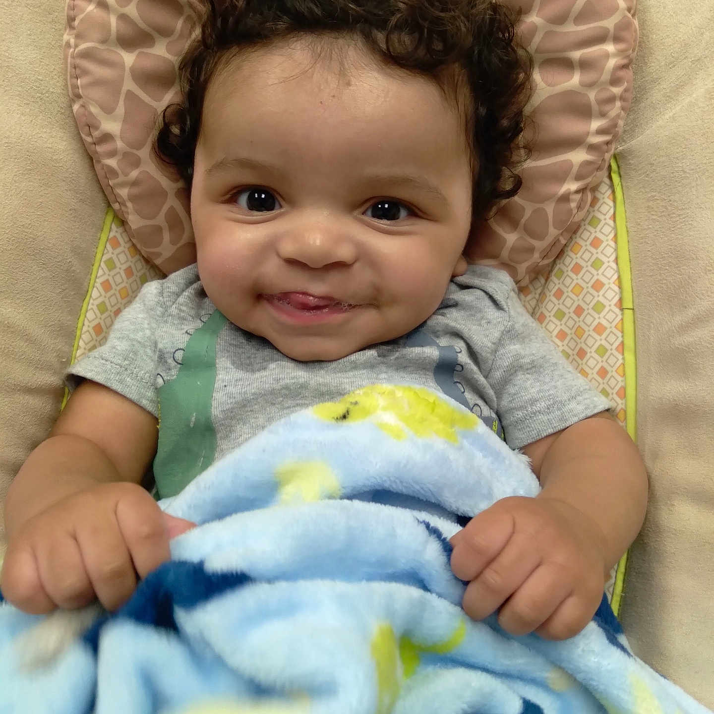 Hyland is registered to the contest to win money with this photo: baby, baby_seat, blanket, blue_blanket, child, closeup, cozy, curly_hair, cute, face, hands, happy, indoor, infant, patterned_blanket, playful, portrait, smiling, soft_texture, toddler