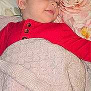 Neriah joined the competition — help win amazing prizes! baby, blanket, child, comfort, cozy, cute, ear, face, flower_pattern, head, indoor, infant, knitwear, pillow, portrait, red_clothing, resting, sleeping_area, smiling, soft_texture