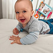 Milo participe au concours pour gagner de l'argent avec cette photo : baby, smiling, infant, bed, crib, toy, blue_clothing, gray_shirt, child, happy, indoor, nursery, cute, playful, young_child, pale_skin, light_hair, toddler, person, face
