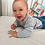 baby, smiling, infant, bed, crib, toy, blue_clothing, gray_shirt, child, happy, indoor, nursery, cute, playful, young_child, pale_skin, light_hair, toddler, person, face