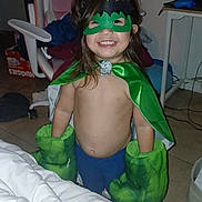 Ivey Codova joined the competition — help win amazing prizes! blanket, boxing_gloves, child, costume, floor_tiles, furniture, gaming_chair, green_cape, green_mask, happy, indoor, person, playful, portrait, room, smiling, superhero_costume, table, toy, young_child