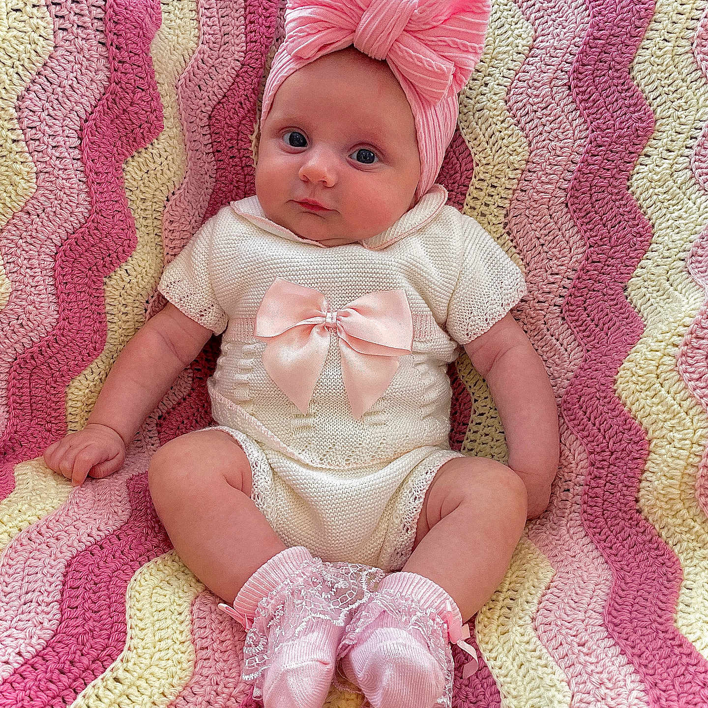 Céline is registered to the contest to win money with this photo: adorable, baby, baby_fashion, child, clothing, colorful, crochet_blanket, cute, headwrap, indoors, infant, knitwear, pattern, pink_bow, portrait, seated, smiling, socks, soft_texture, warm