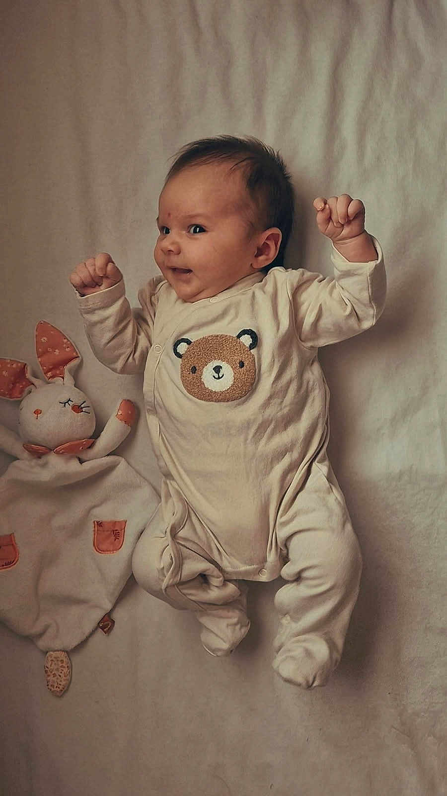 Noëlie participe au concours pour gagner de l'argent avec cette photo : baby, infant, onesie, bear_design, plush_toy, bunny_toy, blanket, soft_texture, cute, smiling, lying_down, child, indoors, cozy, playful, small_hands, sleepy_toy, comfort, adorable, portrait