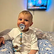 Damir Bivol participe au concours pour gagner de l'argent avec cette photo : baby, pacifier, child, white_outfit, blue_floral_pants, sitting, indoor, face, hand, toy, comfort, television, blurred_background, cute, young_child, happy, portrait, soft_light, home, room