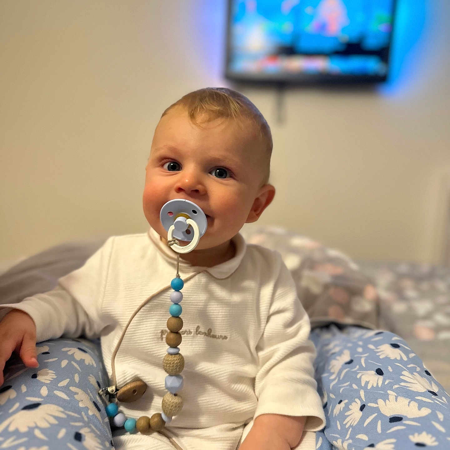 Damir Bivol participe au concours pour gagner de l'argent avec cette photo : baby, blue_floral_pants, blurred_background, child, comfort, cute, face, hand, happy, home, indoor, pacifier, portrait, room, sitting, soft_light, television, toy, white_outfit, young_child
