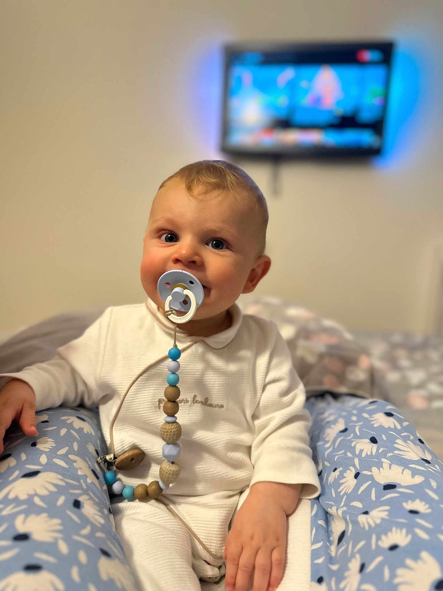 Damir Bivol participe au concours pour gagner de l'argent avec cette photo : baby, pacifier, child, white_outfit, blue_floral_pants, sitting, indoor, face, hand, toy, comfort, television, blurred_background, cute, young_child, happy, portrait, soft_light, home, room