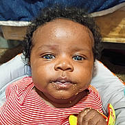 Zyaire is registered to the contest to win money with this photo: baby, child, face, curly_hair, blue_eyes, red_striped_shirt, toy, hand, food_smudges, high_chair, indoor, portrait, infant, cute, person, looking_at_camera, skin, expression, seated, closeup
