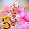 baby, child, infant, smiling, happy, birthday, number_five, balloons, pink, golden_balloon, flower_headband, floral_dress, portrait, indoor, party, celebration, play_mat, sitting, face, photography