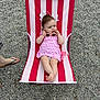 baby, child, sunglasses, beach_chair, striped, pink_dress, outdoor, pebbles, footwear, sandal, person, summer, relaxing, toy, cute, infant, casual, expression, barefoot, vacation