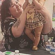 Anita joined the competition — help win amazing prizes! baby, bow, chair, child, curly_hair, face, footwear, happy, holding, indoor, paper, person, plaid_dress, shorts, skin, smiling, table, tattoo, water_bottle, woman