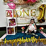 baby, balloons, banner, birthday, blue_fur, celebration, child, cute, decorations, dress, first_birthday, flowers, gold_balloon, indoors, money, party, person, pink, smiling, table
