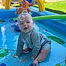 baby, child, swimsuit, inflatable_pool, water, bubbles, toy, green, yellow, blue, outdoor, grass, sunlight, play, fun, summer, animal_toy, smiling, sitting, backyard