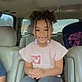 child, girl, smile, braided_hair, hair_beads, car_interior, leather_seat, car_seat, armrest, window, portrait, hands, sitting, pink_shirt, gray_pants, happy, curly_hair, family_trip, passenger, vehicle