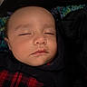 baby, sleeping, infant, face, portrait, blanket, bundled, swaddled, indoors, cozy, peaceful, closed_eyes, dark_clothing, red_plaid, textile, resting, head, child, closeup, photography