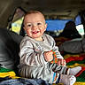 Theodore is registered to the contest to win money with this photo: baby, child, smiling, toy, beads, knitted_blanket, colorful, sitting, cozy, vehicle_interior, happy, cute, casual_clothing, sock, portrait, indoor, playful, infant, expression, warm