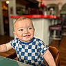 child, toddler, smile, face, indoor, checkered_shirt, blue_shirt, short_hair, seated, table, wooden_chair, happy, curious, portrait, person, baby, cute, young_child, home, blurred_background