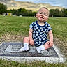 baby, child, smiling, grass, gravestone, cemetery, outdoor, mountain, sky, clouds, blue_clothing, checkered_pattern, socks, person, nature, portrait, happy, sitting, greenery, daytime