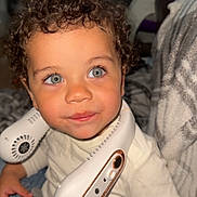 Cohen is registered to the contest to win money with this photo: blanket, blue_eyes, casual_clothing, child, cozy, curly_hair, cute, furniture, home, indoor, jeans, neck_fan, person, portrait, sitting, smiling, technology, toddler, white_shirt, young_child