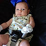 arms, baby, baby_seat, black_background, blue_bow, child, curious, floral_outfit, headband, indoors, infant, legs, person, portrait, puzzled_expression, seatbelt, skin, strapped_in, white_mittens, wide_eyes