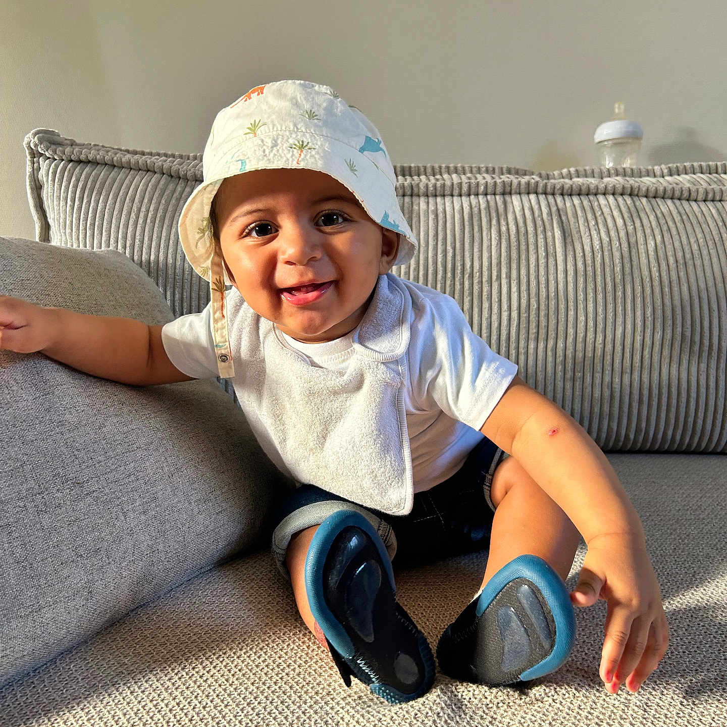 Laye a rejoint le concours — aidez-le/la à gagner de superbes lots ! baby, bib, bucket_hat, casual, child, clothing, couch, cozy, cute, footwear, happy, home, indoor, infant, person, playful, sitting, smiling, sunlight, young_child