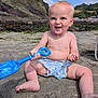 Albert is registered to the contest to win money with this photo: baby, toddler, child, beach, sand, blue_shovel, smiling, barefoot, summer, outdoor, nature, hill, rocky_cliff, sky, clouds, sunny, play, shorts, happy, vacation