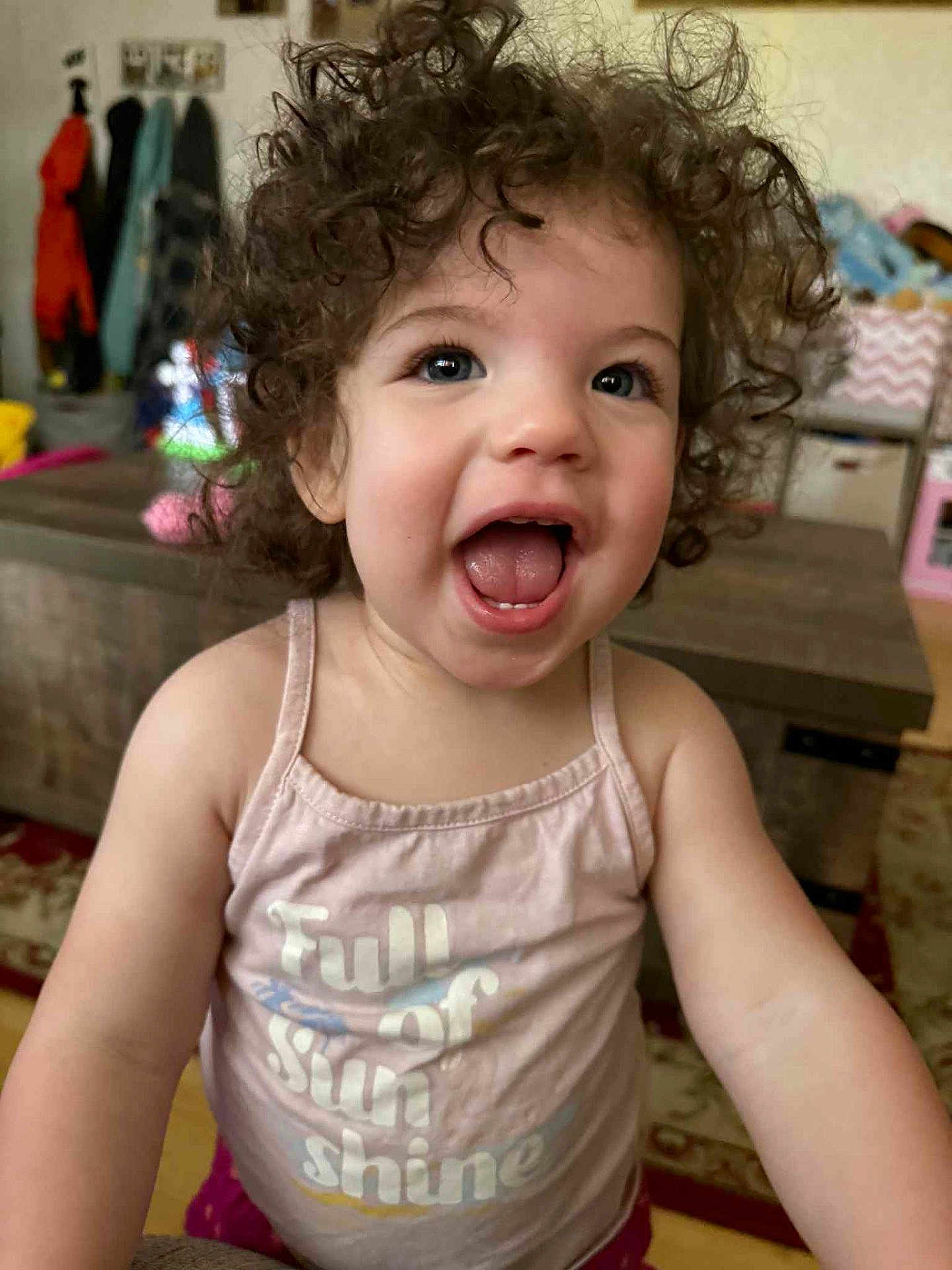 Trinity is registered to the contest to win money with this photo: toddler, child, curly_hair, smiling, pink_tank_top, indoor, happy, face, person, clothing, expression, cute, portrait, young_child, playful, home, furniture, colorful, joy, cheerful