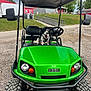 dog, french_bulldog, golf_cart, green_vehicle, outdoor, gravel, grass, red_building, gray_building, side_mirror, wheel, steering_wheel, seat, pet, canine, sunny, daytime, sky, happy, animal