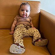 Kaylanna joined the competition — help win amazing prizes! baby, child, infant, leopard_print, pants, brown_top, headband, bow, leather_couch, indoor, sitting, footwear, shoes, cute, smile, face, person, cozy, curious, comfortable