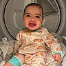 baby, child, smiling, pajamas, rainbow_pattern, laundry, dryer, appliance, indoors, white_clothes, cute, happy, infant, sitting, face, clothing, home, playful, bright, clean