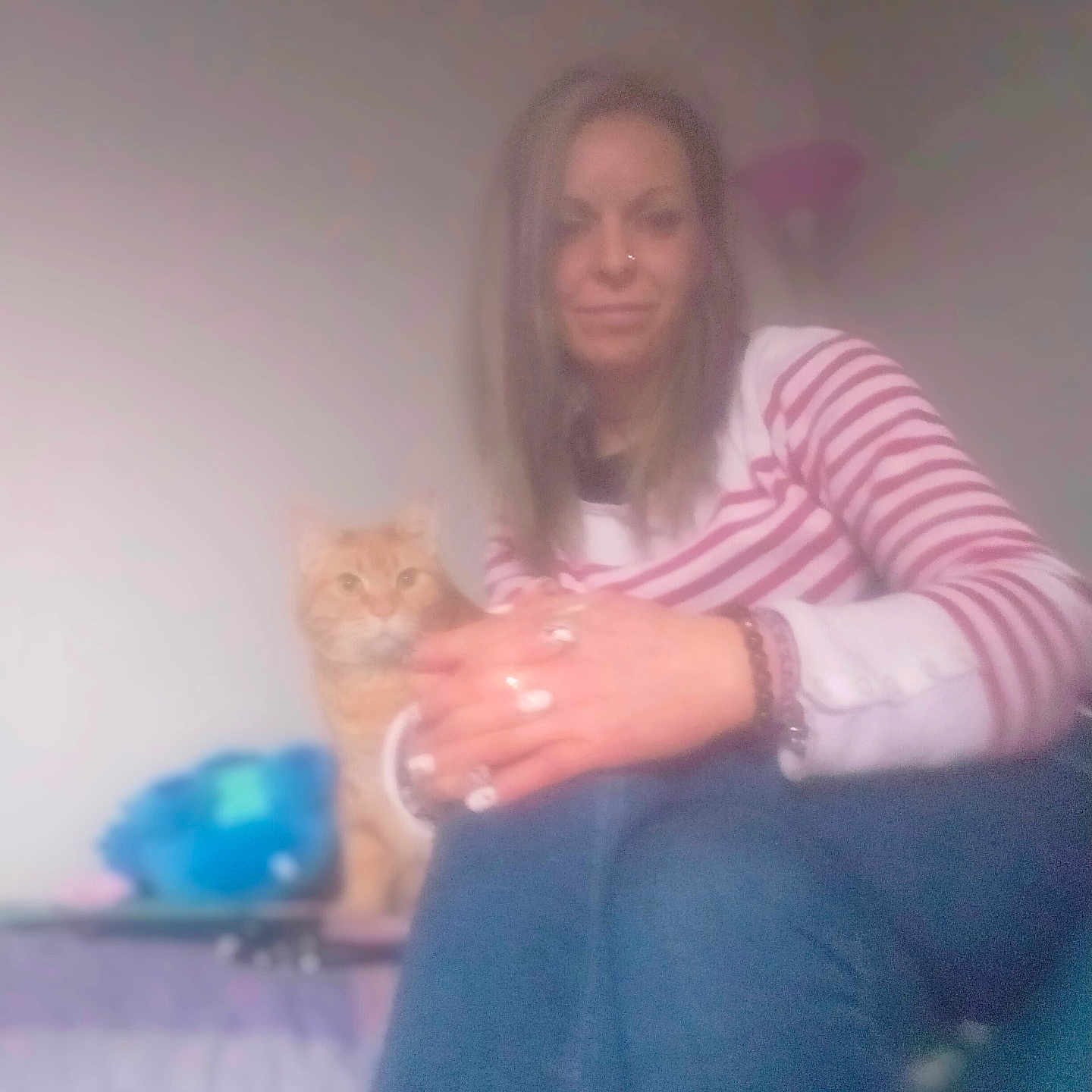 Garfield participe au concours pour gagner de l'argent avec cette photo : woman, cat, striped_shirt, jeans, indoor, lamp, seated, pet, ginger_cat, curious, blurry, casual, home, hands, nail_polish, bracelet, portrait, relaxed, furniture, soft_focus