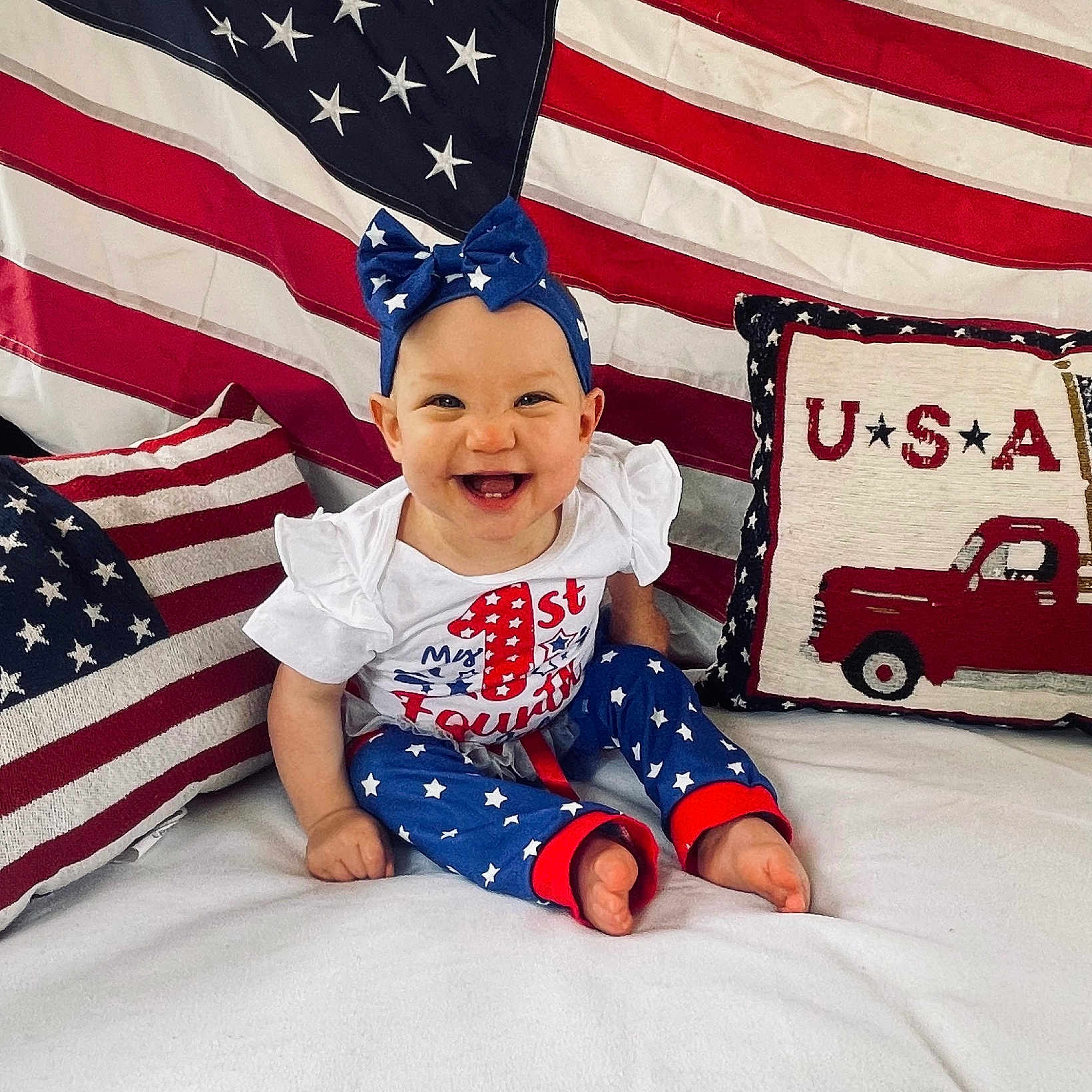 Emma is registered to the contest to win money with this photo: americanflag, baby, babylaughing, car, couch, cushion, face, flag, furniture, happy, head, homedecor, machine, person, photography, portrait, sitting, transportation, vehicle, wheel