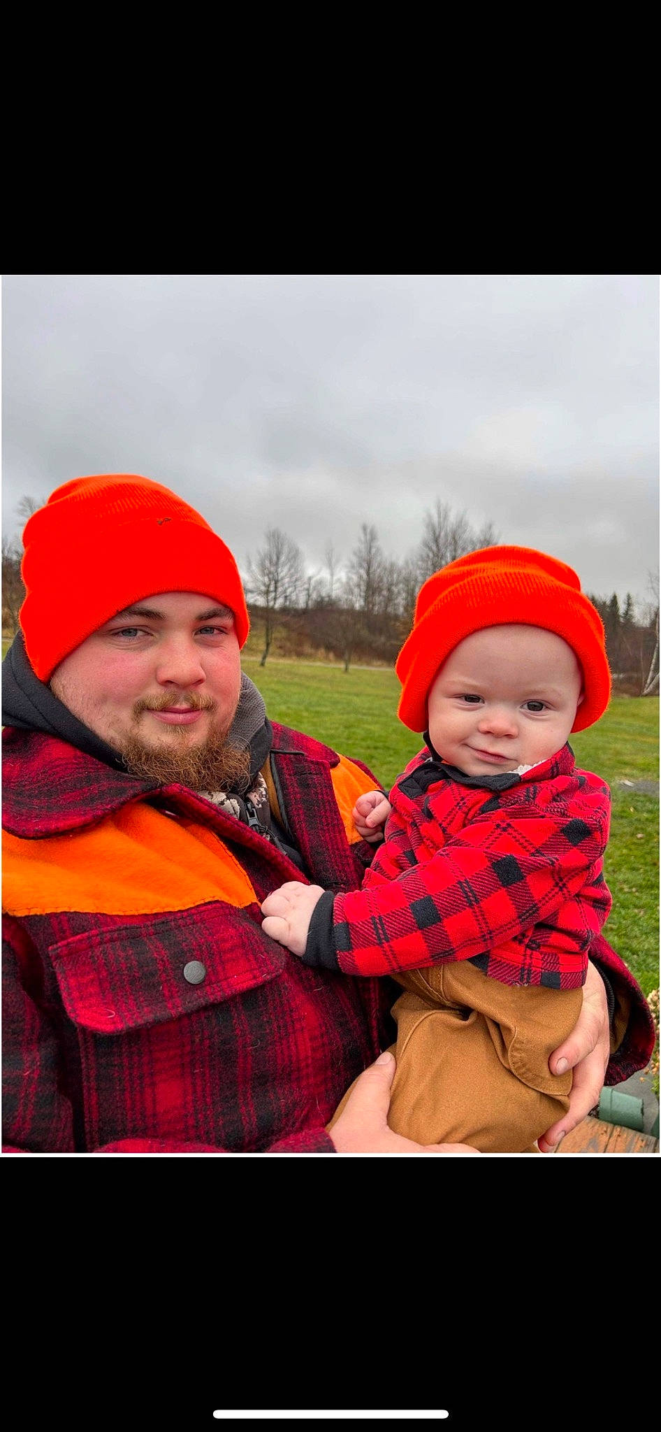 Johnny is registered to the contest to win money with this photo: baby, beard, cap, clothing, cloud, facial_expression, fun, grass, happy, headwear, jacket, joy, outerwear, people_in_nature, person, plaid, plant, red, sky, smile