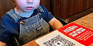 Axel joined the competition — help win amazing prizes! toddler, child, blue_eyes, overalls, striped_clothing, high_chair, restaurant, table, placard, qr_code, pizza_ranch, face, curious, messy, food, indoor, wood_paneling, person, clothing, seat