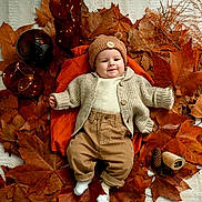 Jules a rejoint le concours — aidez-le/la à gagner de superbes lots ! autumn, baby, brown_leaves, cardigan, child, corduroy_pants, cozy_clothing, cute, decorative_jars, fall_leaves, indoors, knit_hat, laying_down, nature, orange_blanket, pinecones, portrait, seasonal, smiling, socks