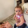 child, baby, toddler, indoor, person, floor, tile_floor, clothing, woman, hand, curly_hair, jeans, shirt, smile, playful, holding, sitting, heater, face, family