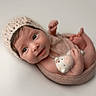 baby, newborn, infant, blanket, knitted_bonnet, plush_toy, soft_texture, cute, portrait, child, wrapped, smiling, small_hands, small_feet, lying_down, studio_lighting, neutral_background, adorable, innocent, closeup