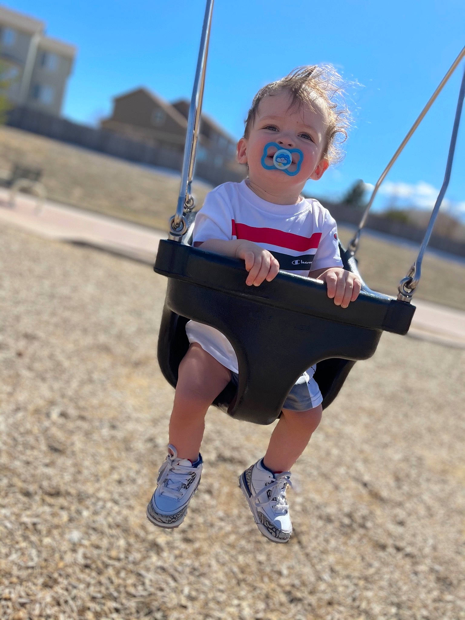 Desmond is registered to the contest to win money with this photo: automotive_wheel_system, clothing, electric_blue, fun, hand, happy, human_body, leisure, outdoor_play_equipment, outdoor_recreation, people_in_nature, person, recreation, shorts, sky, sneakers, swing, toddler, travel, tree