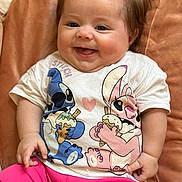 Mattéa a rejoint le concours — aidez-le/la à gagner de superbes lots ! baby, child, smiling, happy, tshirt, pink_shorts, cushion, brown_background, cute, infant, portrait, indoors, chubby_cheeks, sitting, clothing, person, cute_expression, shorts, soft_texture, joy