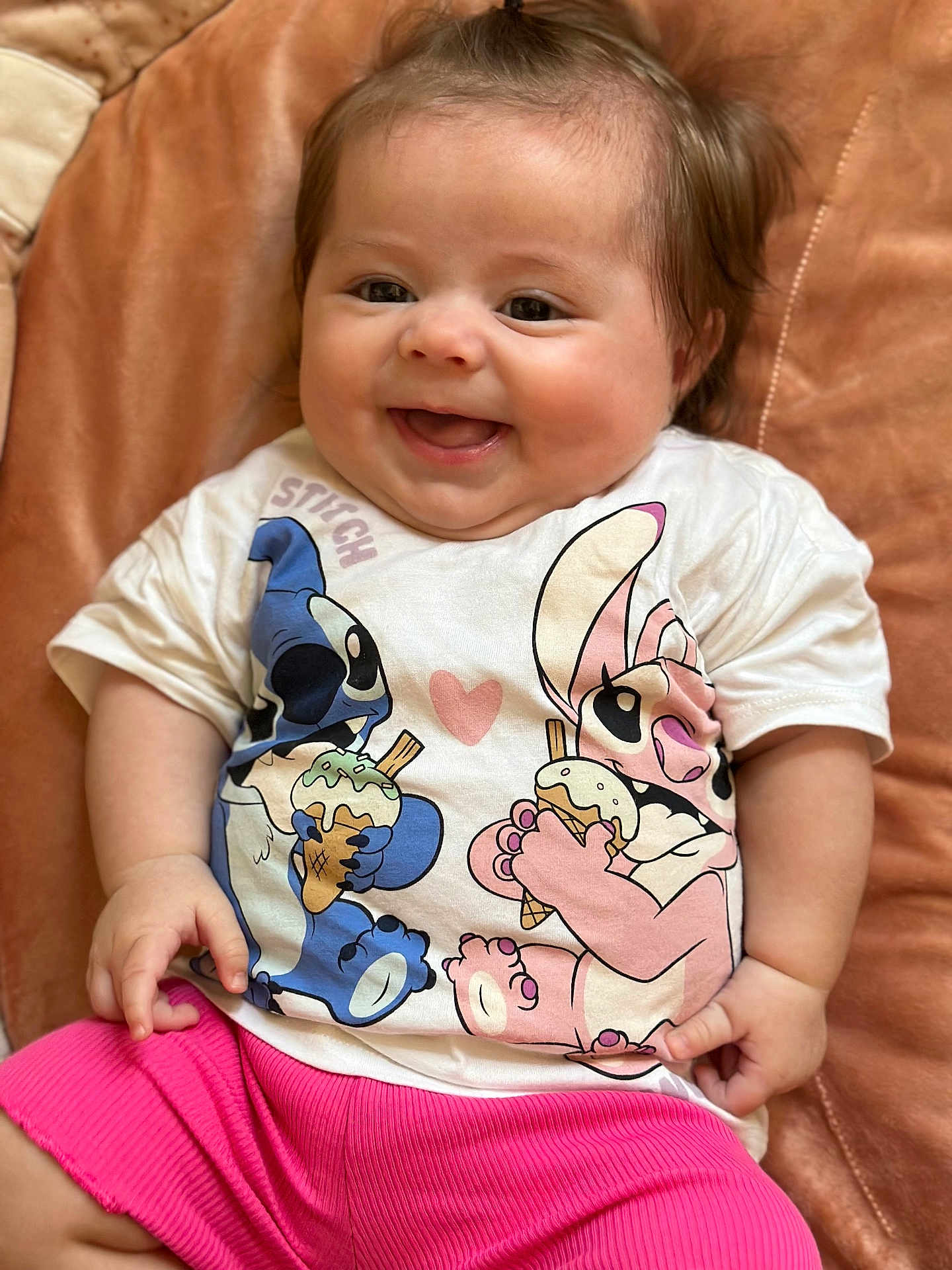 Mattéa a rejoint le concours — aidez-le/la à gagner de superbes lots ! baby, child, smiling, happy, tshirt, pink_shorts, cushion, brown_background, cute, infant, portrait, indoors, chubby_cheeks, sitting, clothing, person, cute_expression, shorts, soft_texture, joy