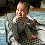 baby, child, smiling, curly_hair, grey_clothing, fabric_basket, blue_rug, indoor, wooden_floor, playroom, toy_in_background, happy, cute, sitting, foot, hand, face, person, home, cozy