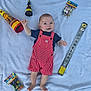 baby, infant, child, red_striped_overalls, blue_shirt, party_poppers, sparklers, blanket, smile, happy, celebration, colorful, footwearless, lying_down, cute, party, small_hands, soft_texture, indoors, playful