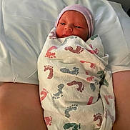 Josiah is registered to the contest to win money with this photo: newborn, baby, blanket, footprint_pattern, pink_hat, swaddled, pillow, resting, infant, person, human, skin, face, headwear, hospital, bed, arm, closeup, indoors, soft_lighting