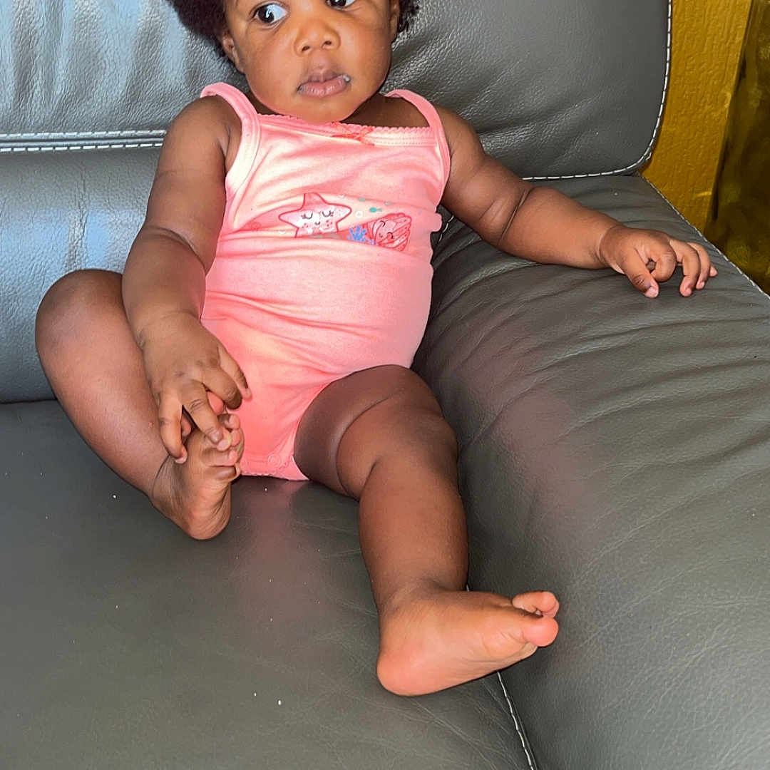 Majalys participe au concours pour gagner de l'argent avec cette photo : afro, baby, casual, child, comfortable, couch, curious, expression, foot, furniture, hand, home, indoor, leather, pink_onesie, relaxed, sitting, skin, toddler, young_child